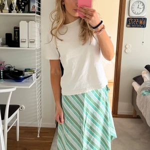 Grön och vit randig omlottkjol - Säljer en somrig grön och vit randig omlottkjol med knytning i midjan. Kjolen har en luftig passform och är perfekt för varma dagar. Den har en elegant omlottdesign som ger en fin siluett.