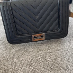 Svart quiltad axelväska - Snygg svart axelväska med quiltat mönster och silverfärgad kedja. Väskan har en praktisk dragkedja inuti och ett stilrent spänne framtill. Perfekt för att bära med sig det viktigaste med stil.