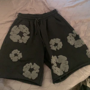 Svarta Denim Tears shorts - .Snygga svarta shorts från Denim Tears med ett unikt blommönster i vitt. De har en bekväm resårmidja med snörning för perfekt passform. Perfekta för en avslappnad stil