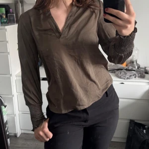 Olivgrön blus med  - Snygg olivgrön blus med v-ringning och smockdetaljer vid ärmsluten. (Katt och kanin finns i hemmet) 