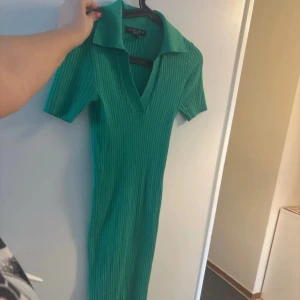 Grön ribbad klänning från Amisu - Snygg grön ribbad klänning från Amisu med krage och v-ringning. Klänningen har korta ärmar och en figurnära passform. Perfekt för en stilren look!