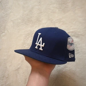 Blå keps från New Era - Säljer en väldigt sällsynt blå keps från New Era med broderade detaljer och logotyper för Dodgers och Dodger Stadium. Kepsen har en platt skärm och flera broderade märken runtom, vilket ger den en unik look. Hör av dig vid funderingar och pris kan diskuteras vid snabb affär mvh Malte.202