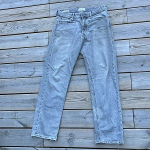 Grå jeans från Jack & Jones - Snygga grå jeans från Jack & Jones med en relaxed passform. De har en klassisk femficksdesign och en knappgylf. Storlek 28/30 och passar dig som är 170 till 185 centimeter lång.