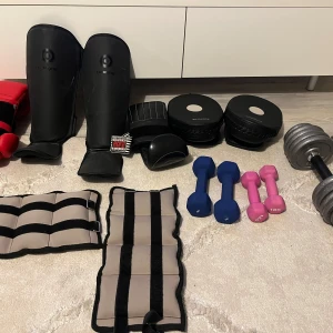 Träningsutrustning med vikter och skydd - Samling av träningsutrustning inklusive vikter i olika färger och storlekar, samt skyddsutrustning som benskydd och handledsskydd. Perfekt för hemmaträning eller gymmet.