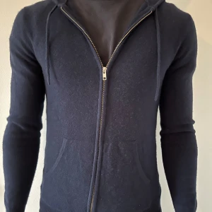 Mörkblå kashmere  med dragkedja - Säljer en stilren mörkblå hoodie med dragkedja och huva. Tröjan har långa ärmar och praktiska fickor framtill. Perfekt för en avslappnad look.