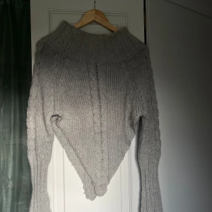 Stickad poncho - En grå stickad poncho med klickade ärmar och hög krage. Storlek m.
