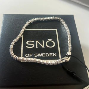 Silverarmband från Snö of Sweden - Elegant silverarmband från Snö of Sweden med fyrkantiga länkar och gnistrande detaljer. Perfekt för att ge en stilren touch till din outfit. Levereras i originalförpackning.