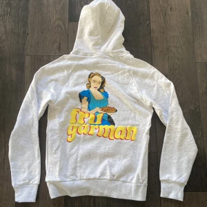 Revenite Hoodie - Snygg ljusgrå hoodie med en stor färgglad tryck på baksidan föreställande en kvinna och texten 'fru gårman'. Hoodien är från Revenite, och var deras sista släpp innan dom slutade. Oanvänd. 