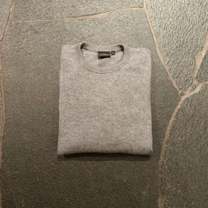 Grå tröja från Oscar Jacobson - Säljer en stilren grå tröja från Oscar Jacobson, tillverkad i Italien. Tröjan har en klassisk rund hals och är perfekt för en elegant vardagslook. Den har en liten röd prick på armbågen. Tillverkad i kahsmir. Nypris: 1399   Mitt pris: 239