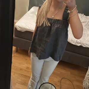 Grå  ärmlös topp - Säljer en stilren ärmlös topp med breda axelband. Perfekt för varma dagar eller som ett lager under en jacka. Toppen har en lös passform som ger en avslappnad look.