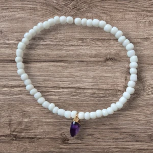 Handgjort armband med vita pärlor och ametistberlock - Detta eleganta armband är handgjort med vita, glansiga pärlor och pryds av en vacker lila ametistberlock infattad i guldfärgad metall. Armbandet har en stilren och tidlös design som passar perfekt både till vardags och till fest. Den elastiska tråden gör det enkelt att ta på och av samtidigt som det sitter bekvämt runt handleden. Ametist sägs symbolisera lugn och balans, vilket gör detta armband till en meningsfull och personlig accessoar.