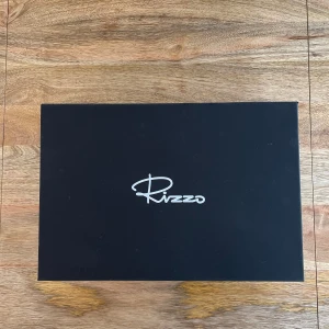 Svarta sandaler med kilklack från Rizzo - Snygga svarta sandaler från Rizzo med kilklack i flätad design. De har en öppen tå och justerbara remmar runt ankeln. Perfekta för sommarens alla tillfällen.