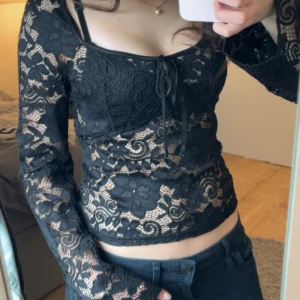 Svart spetsblus  - Snygg svart spetsblus med långa ärmar och knytning framtill. Blusen har ett vackert blommigt mönster och är perfekt till fest och konserter! 🥰pris kan diskuteras!