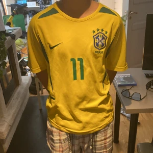 Gul Brasilien fotbollströja med Ronaldinho 11 - Tja säljer nu denna sjukt feta Brasilien fotbollströjan, med Ronaldinho på ryggen. Perfekt till sommaren då ni kommer sticka ut nu med en cool look! Tröjan är helt oanvänd, skick 10/10, pris kan diskuteras här av er vid frågor!