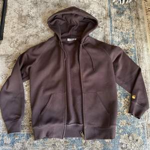 Säljer en brun hoodie från Carhartt med dragkedja och huva i tjockt och tåligt material. Den har långa ärmar och en praktisk ficka framtill. Perfekt för en avslappnad stil. Inga defekter förutom lite sömmar som har gått upp på ena ärmen.