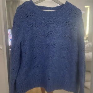 Blå stickad tröja från Pieces - Säljer en blå stickad tröja från Pieces med ett fint hålmönster. Tröjan har långa ärmar och ribbstickade muddar vid ärmslut och nederkant. Perfekt för kyliga dagar!