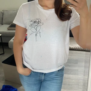 Vit t-shirt med rosdetalj - Säljer en stilren vit t-shirt med en snygg rosdetalj tryckt på bröstet. 