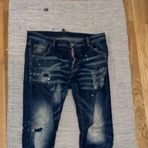 Dsquared2 kom privat - Snygga mörkblå jeans med coola slitningar och färgstänk för en unik look. De har en klassisk femficksdesign och knappgylf. Perfekta för en avslappnad stil.