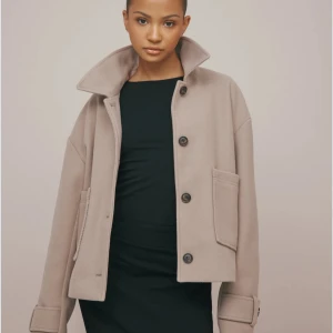 Beige kappa med knappar - Snygg beige kappa med stora knappar och hög krage. Kappan är ifrån Nelly och aldrig använd. Säljer pågrund av att jag fått fel storlek. Kan lösa bilder. Tveksam på storlek 