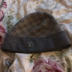 Grå rutig mössa från Louis Vuitton - Snygg grå rutig mössa från Louis Vuitton med ett diskret LV-märke framtill. Perfekt för att hålla stilen under kyliga dagar. Äkta 