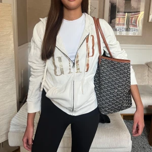 Vit zip hoodie från GAP - Säljer en vit hoodie från GAP med dragkedja och stort tryck i guld och silver på framsidan. Tröjan är köpt i Dubai.