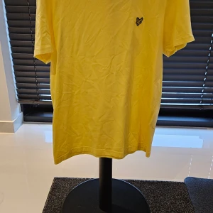 t-shirt Lyle & Scott - Snygg gul t-shirt från Lyle & Scott med korta ärmar och en liten broderad logga på bröstet. Perfekt för en avslappnad stil.