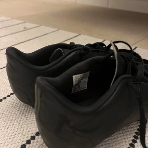 Svarta fotbollsskor från Adidas - Säljer ett par svarta Adidas Predator fotbollsskor med snörning. Skorna har en stilren design och är perfekta för fotbollsplanen. De är tillverkade i syntetmaterial för hållbarhet och prestanda.