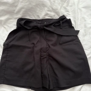 Svarta shorts med knytband - Snygga svarta shorts med hög midja och knytband i midjan. Perfekta för en stilren look. De har en klassisk design med fickor på sidorna. Liten i storlek.