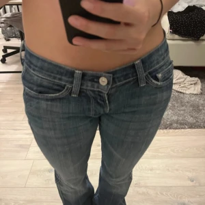 Blå jeans med låg midja - Snygga blå jeans med låg midja och klassisk femficksdesign. Jeansen har en knapp och dragkedja framtill samt dekorativa sömmar på bakfickorna. Perfekta för en avslappnad stil. Midjemått är ca 36 cm och innerben ca 77 cm. Väldigt snygga men tyvärr för små för mig! Kan gå ner i pris vid snabb affär!