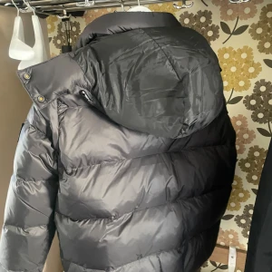 Svart pufferjacka från Calvin Klein  - Säljer en snygg svart pufferjacka från Calvin Klein Jeans. Jackan har en hög krage och en praktisk dragkedja framtill. Den är perfekt för kyliga dagar och har en stilren design med märkets logga på bröstet och ärmen.