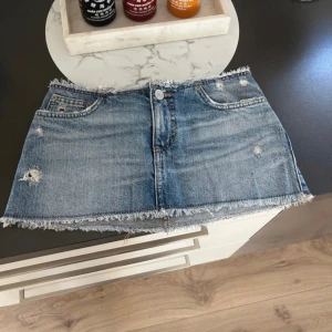 Blå jeanskjol - Snygg blå jeanskjol med slitna detaljer och fransig kant. Kjolen har en klassisk femficksdesign och knäppning fram. Perfekt för en avslappnad stil.