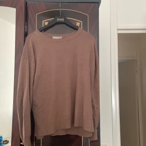 Brun tröja från Fransa - Säljer en brun tröja från Fransa med långa ärmar och dekorativa knappar vid ärmsluten. Tröjan har en rund halsringning och är tillverkad i ett mjukt material som passar perfekt för kyligare dagar.