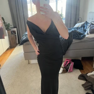 Svart långklänning med öppen rygg - Elegant svart långklänning med en djup v-ringning och öppen rygg. Klänningen har en smickrande passform och är perfekt för festliga tillfällen. 