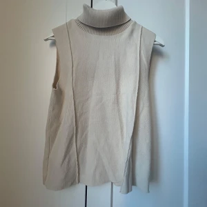 Beige ärmlös polotröja - Säljer en stilren beige ärmlös polotröja med ribbad krage. Perfekt för lager-på-lager eller som den är. Passar både till vardag och mer uppklädda tillfällen.