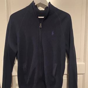Ralph Lauren zip tröja  - Säljer en stilren mörkblå tröja från Polo Ralph Lauren. Tröjan har en dragkedja framtill och långa ärmar. Perfekt för en avslappnad och snygg look.