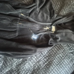 Svart hoodie från Juicy Couture - Säljer en svart hoodie från Juicy Couture med dragkedja och huva. Den har en glittrig Juicy-logga på ryggen och långa ärmar.Den har en missfärgning på ena armen se bild.
