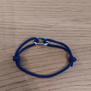 Blått armband med silverdetalj - Snyggt och enkelt blått armband med en justerbar design. Armbandet har en silverfärgad detalj i mitten och knutar för att justera storleken. Perfekt för en stilren look.