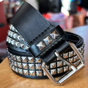 Svart nitbälte vintage/Y2K! - Svart 3-radigt nibälte i vintage/Y2K-stil med pyramidnitar. Mått: L: 110 cm (80-95 cm innersta och yttersta hålet). B: 4 cm. Nytt!