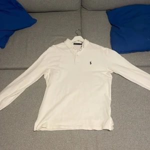 Vit pikétröja från Ralph Lauren - Säljer en klassisk hel vit pikétröja från Ralph Lauren med lång ärm och den ikoniska loggan broderad i mörk blå på bröstet. Tröjan har en krage och knappar vid halsen.  Nypris ca(1500kr) säljer billigare eftersom den inte passar mig längre, pris kan sänkas om du har ett bra förslag. Hämtas i person