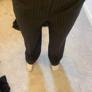 Randiga kostymbyxor från NA-KD - Snygga kostymbyxor från NA-KD i en klassisk svart/grå färg med  ränder. Byxorna har en rak passform och är perfekta för en stilren look. Tillverkade i ett bekvämt material som ger en elegant känsla.
