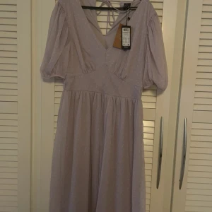 Ljuslila prickig klänning från Vero Moda - Säljer en söt ljuslila klänning från Vero Moda med vita prickar. Klänningen har en v-ringad design och korta ärmar. Perfekt för våren/sommaren!🌼🌸aldrig använd!