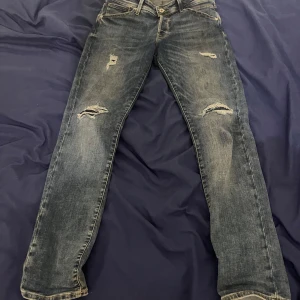 Blå Jack and Jones jeans - Snygga blå jeans med slitna detaljer och en slim passform. De har en klassisk femficksdesign och är perfekta för en avslappnad stil. Midjemått är 31 och längden 32.