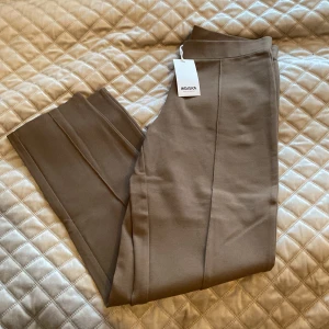 Bruna byxor från Indiska - Snygga bruna byxor från Indiska med hög midja och rak passform. Perfekta för en stilren look. Byxorna har en enkel design utan mönster och är tillverkade i ett mjukt material.