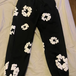 Svarta denim tears byxor med vita blommor - Snygga svarta denim tears byxor med vita blommönster. Perfekta för en unik och stilren look. Byxorna har en bekväm passform och är lätta att matcha med olika toppar.