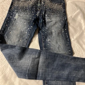 Super snygga  jeans med glittriga stenar - Snygga blå jeans dekorerade med glittriga stenar över hela framsidan. Sitter super snyggt på, har en lätt slitning för en trendig look. Perfekta för att ge din outfit lite extra bling!