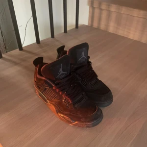 Svarta Nike Air Jordans 4 - Säljer ett par svarta Nike Air Jordans med klassisk design och snörning. Skorna har en ikonisk Jumpman-logga på sulan och är perfekta för både stil och komfort.