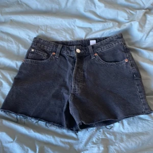 Svarta jeansshorts från HM - Säljer ett par svarta 90-talsinspirerade boyfriend jeansshorts från HM. De är lågmidjade med en avslappnad passform och har fransiga kanter. Perfekta för en cool och avslappnad stil.