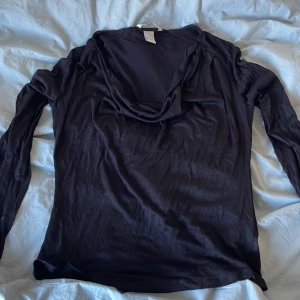 Svart långärmad topp från H&M - Säljer en svart långärmad topp från H&M med en lös passform och en draperad krage. Perfekt för en stilren och bekväm look. Passar bra till både jeans och kjol.