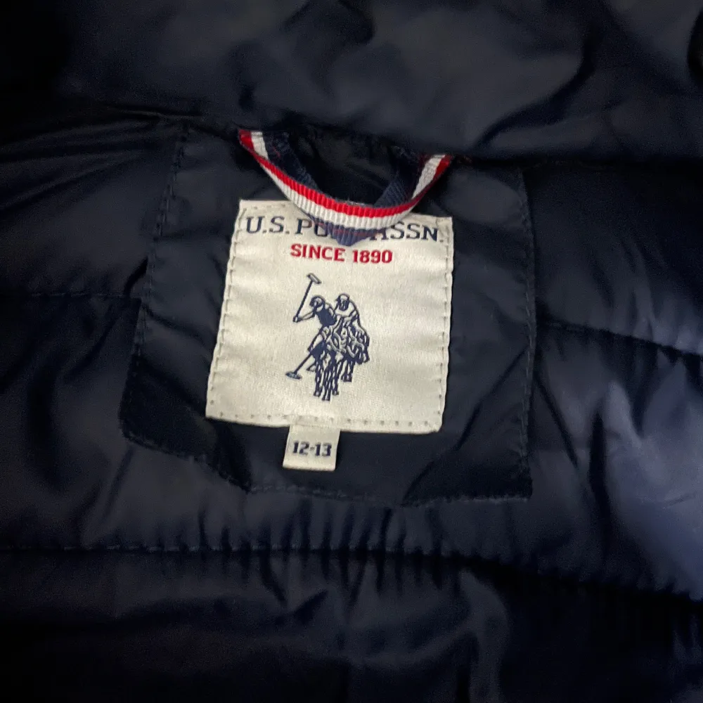 Säljer en snygg mörkblå dunväst från U.S. Polo Assn. med dragkedja och två praktiska fickor framtill. Perfekt för kyligare dagar och ger en stilren look. Passar bra till både jeans och t-shirt. Skriv vid minsta fundering😃. Takit.