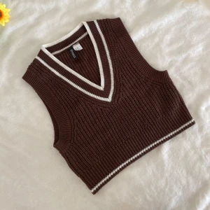 Brun stickad väst från H&M - Snygg brun stickad väst från H&M med vita ränder. Den har en v-ringad design och är perfekt för lager-på-lager-stil. Västen är ribbad och har en croppad passform.